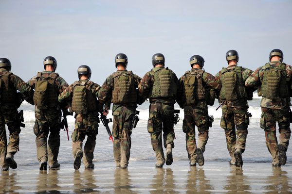 Soldiers walking on beach in tactical gear.